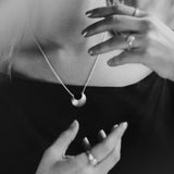Black and white close-up of a person wearing  the Sterling Silver Luna Crescens necklace featuring a crescent moon by Emily Eliza Arotte. The persons hands are in a magical pose around the necklace.