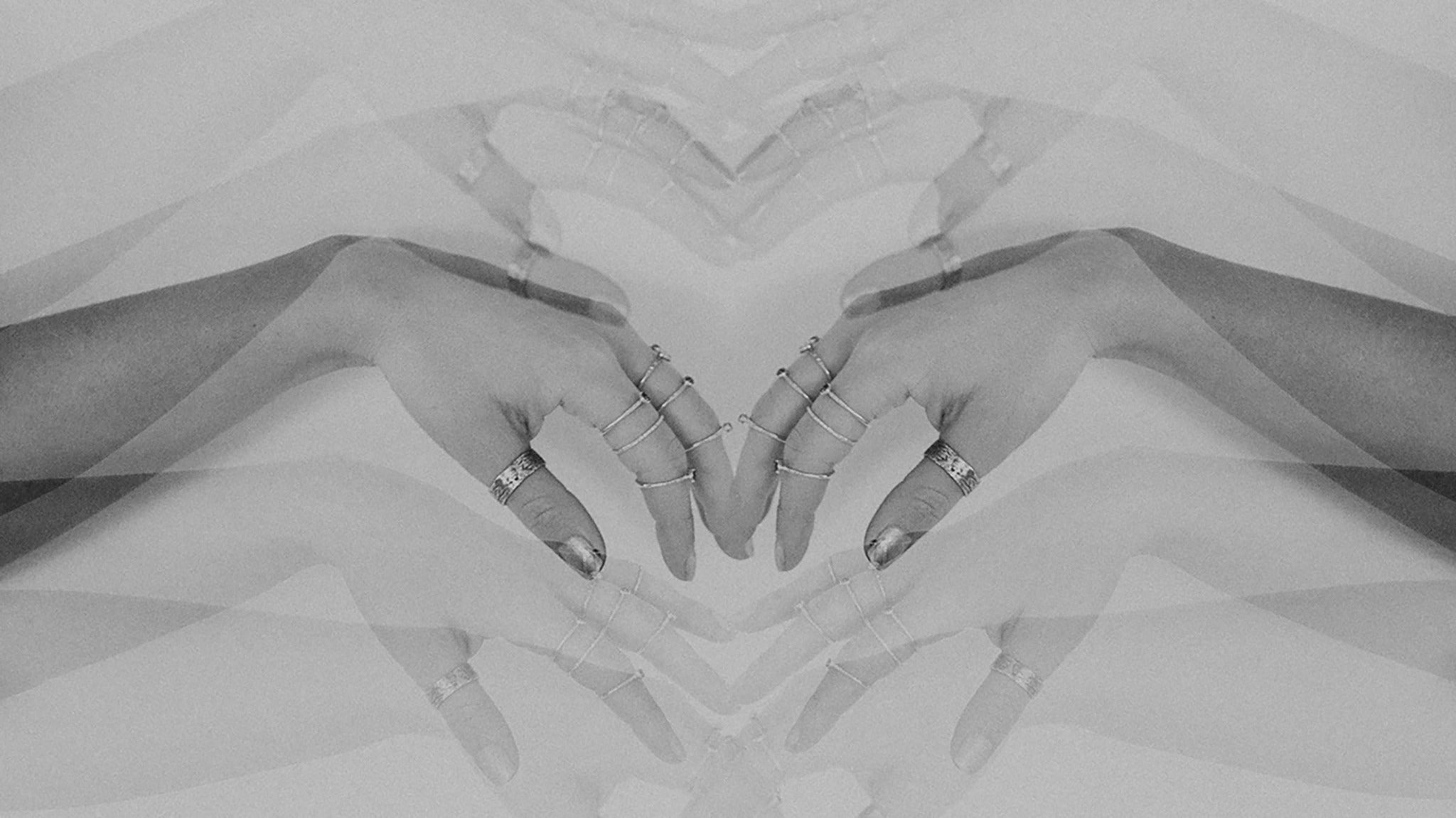 A mirrored image of hands meeting in the middle, wearing a stack of Emily Eliza Arlotte rings.