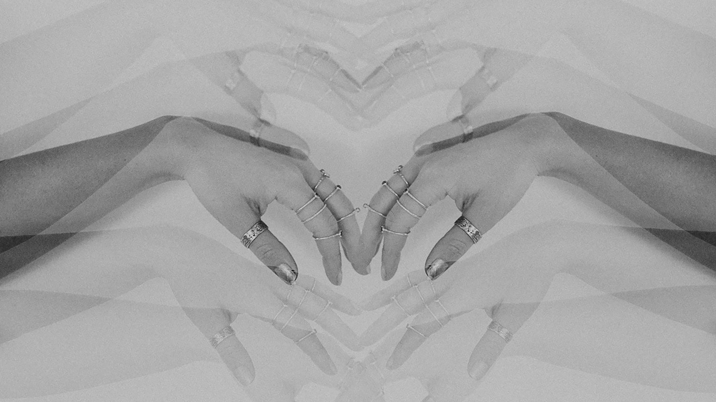 A mirrored image of hands meeting in the middle, wearing a stack of Emily Eliza Arlotte rings.