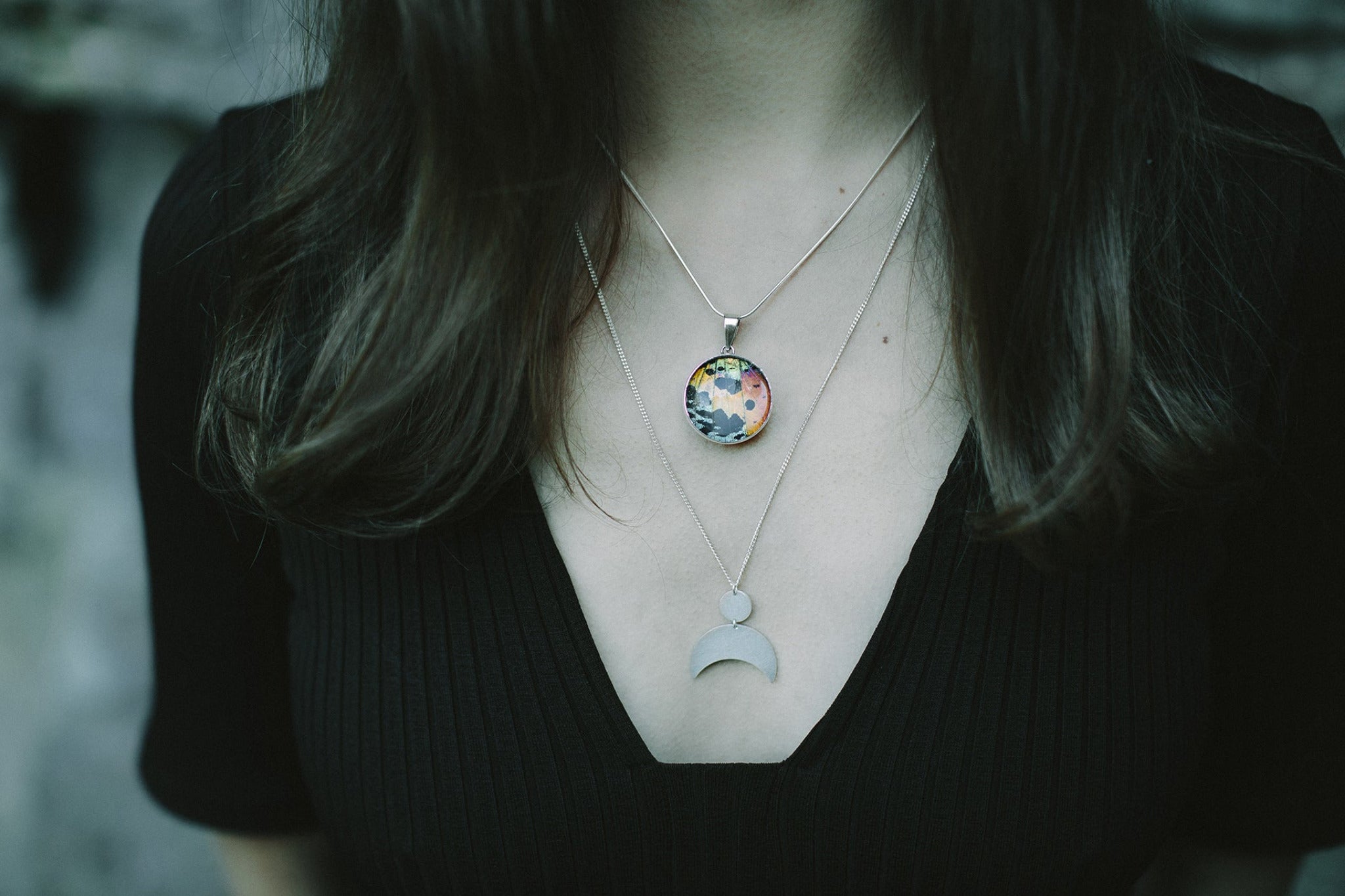 A woman wearing two layered necklaces, a real butterfly wing pendant and a moon goddess pendant.