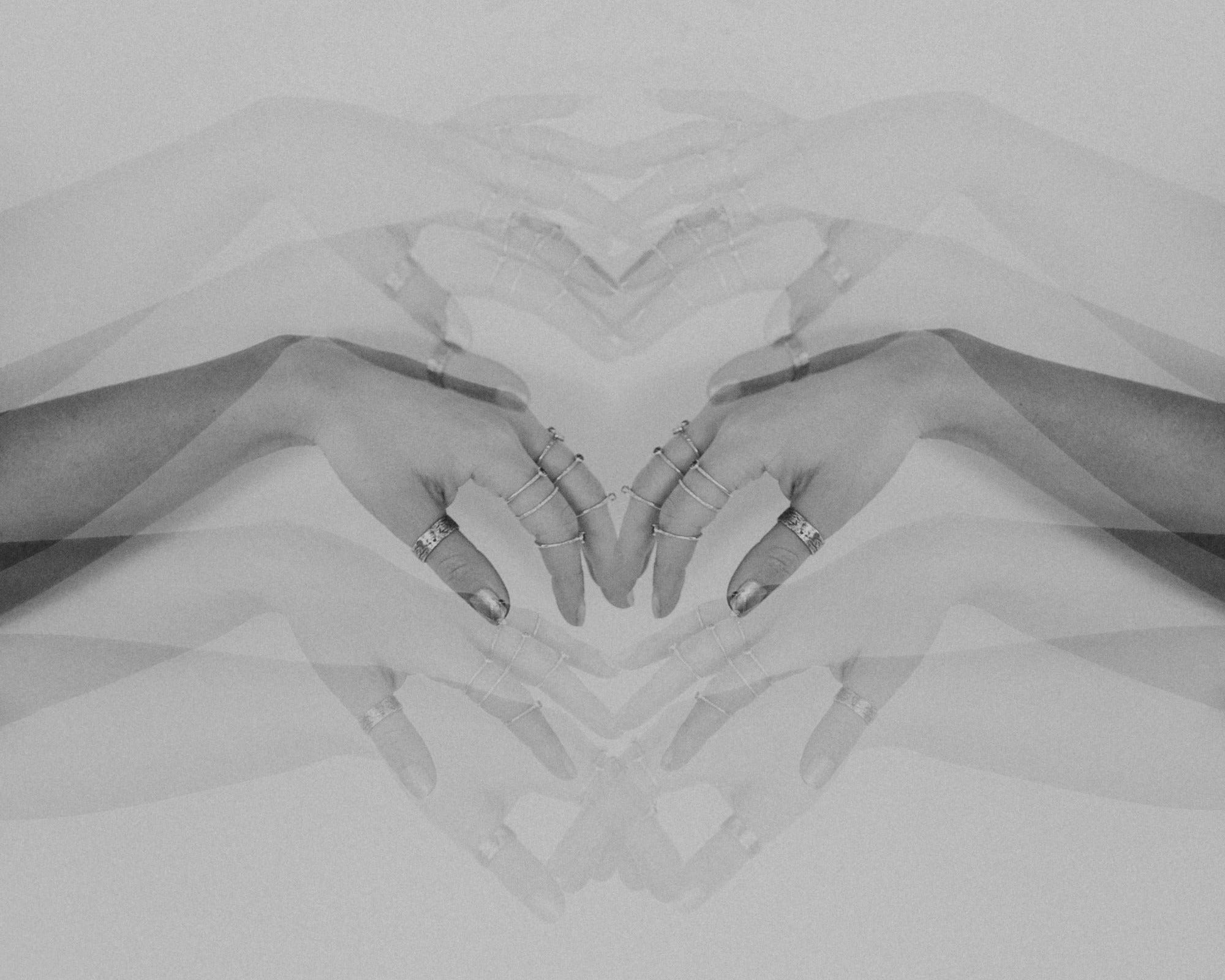Black and white abstract image of hands meeting in the middle of the image, wearing jewellery by Emily Eliza Arlotte. There are multiple exposures on the image.