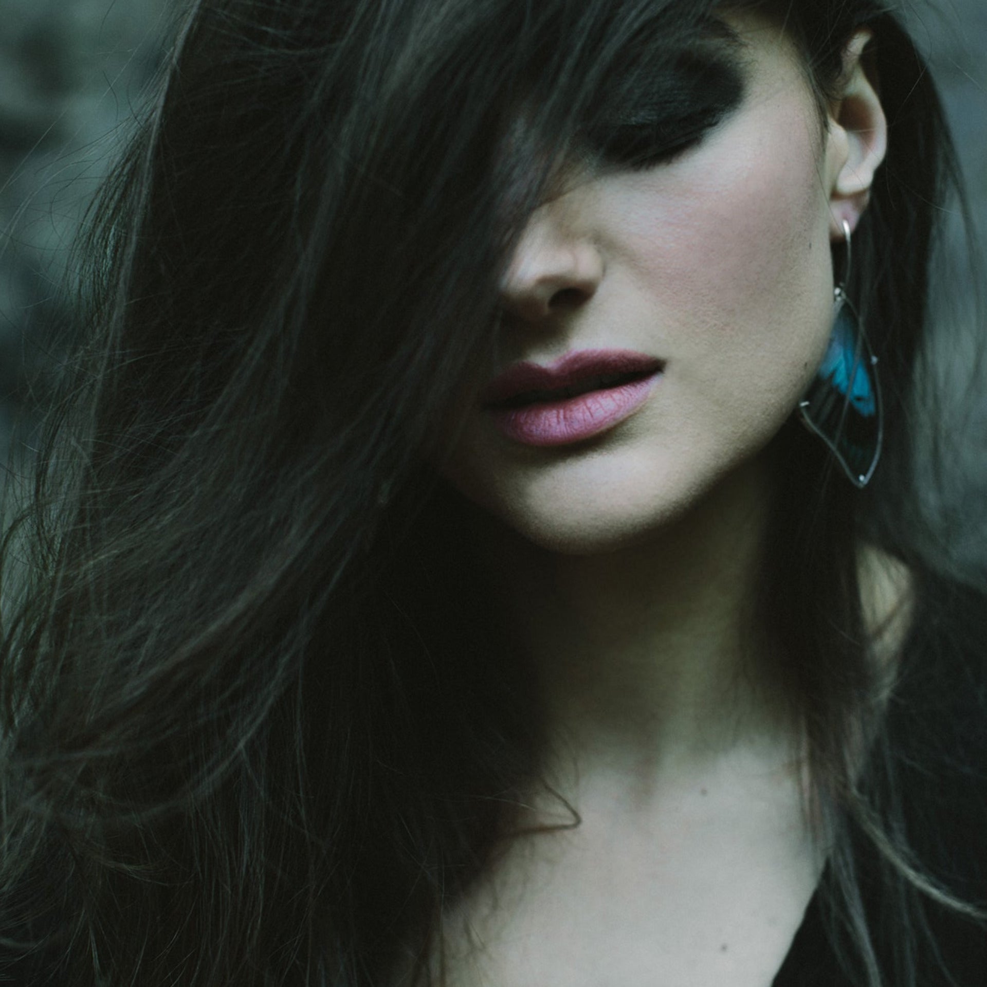 A woman has her hair dramatically swept across her face and is wearing a real blue butterfly wing earring.