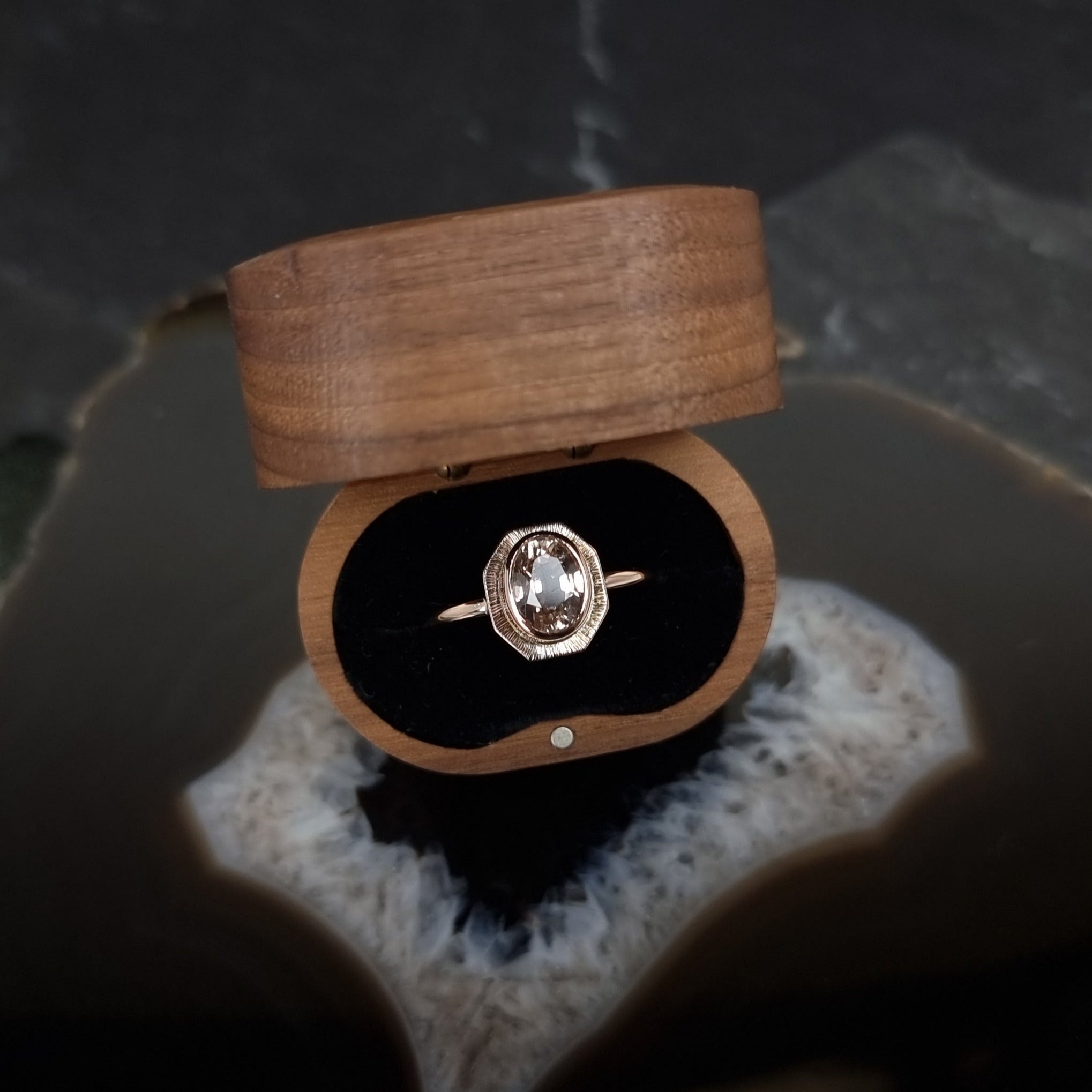 Rose Gold and Diamond ring by Emily Eliza Arlotte in a wooden gift box on a dark stone surface.