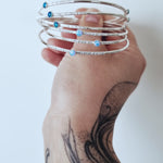 A tattooed hand holds a collection of Sterling Silver Opal Bangles by Emily Eliza Arlotte