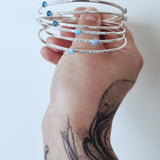 A tattooed hand holds a collection of Sterling Silver Opal Bangles by Emily Eliza Arlotte