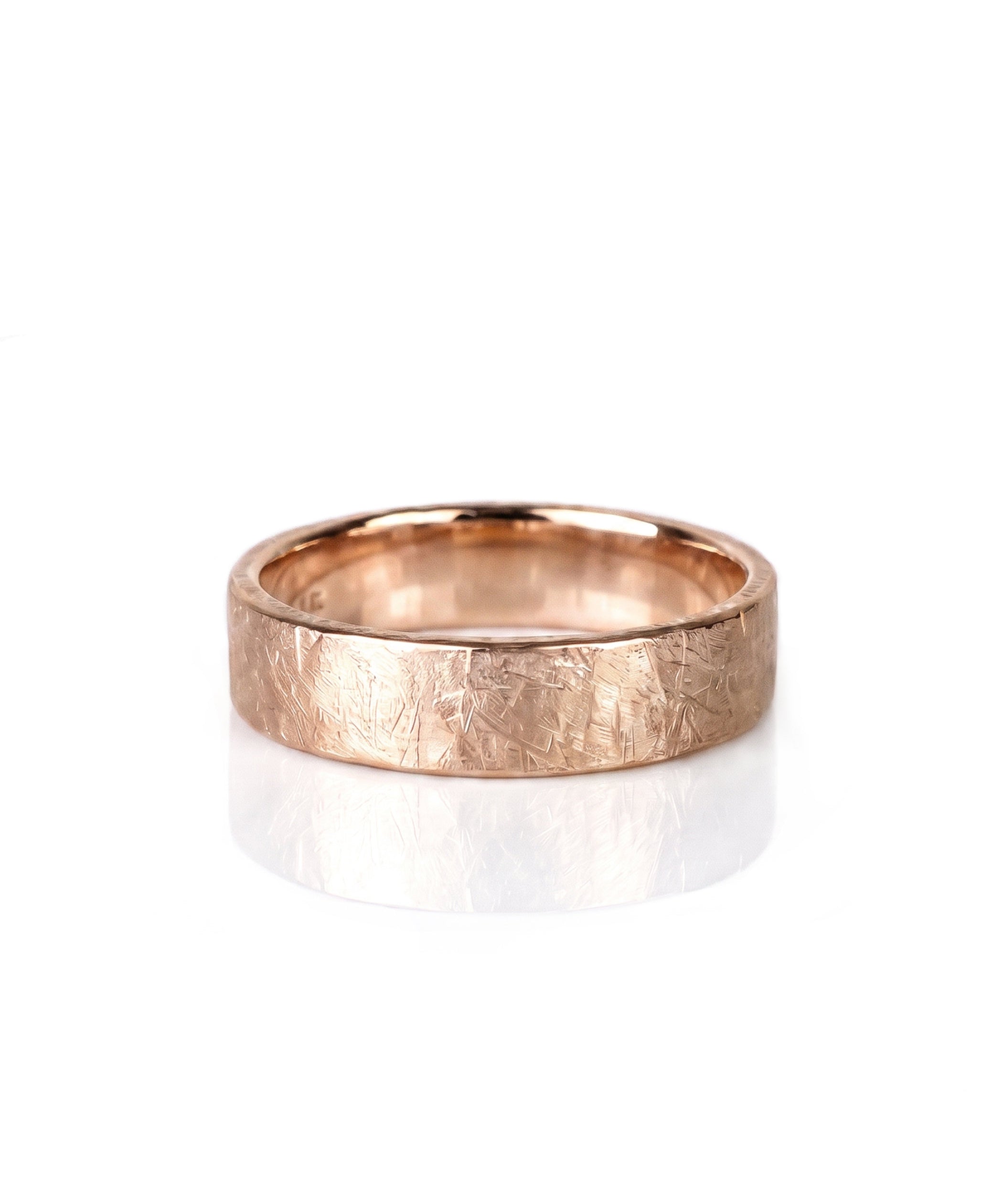 A textured rose gold wedding band ring with a hammered, crisscrossed finish, shown on a clean white background with a soft reflection. Handmade by Emily Eliza Arlotte in Hobart, Tasmania.