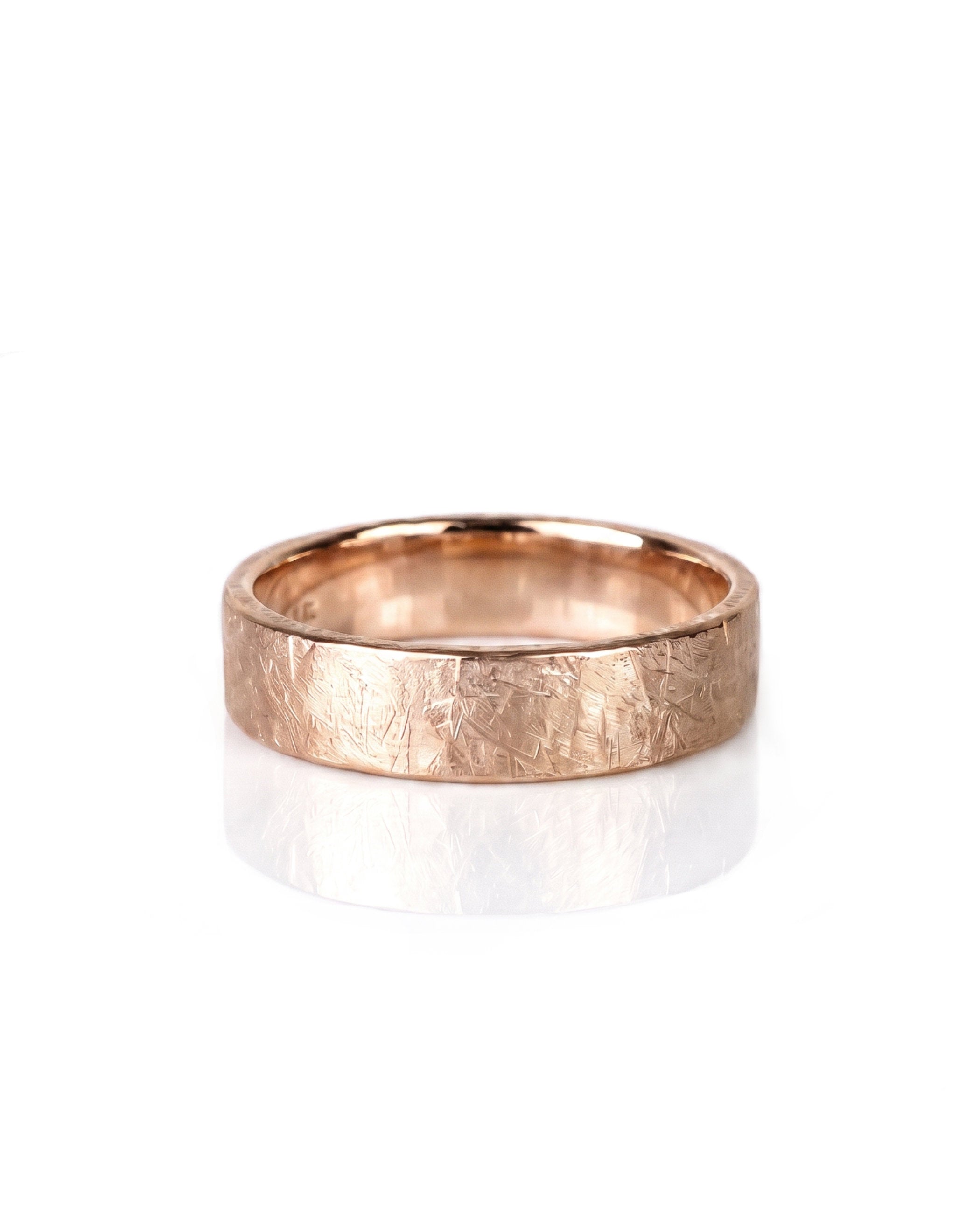 A textured rose gold wedding band ring with a hammered, crisscrossed finish, shown on a clean white background with a soft reflection. Handmade by Emily Eliza Arlotte in Hobart, Tasmania.
