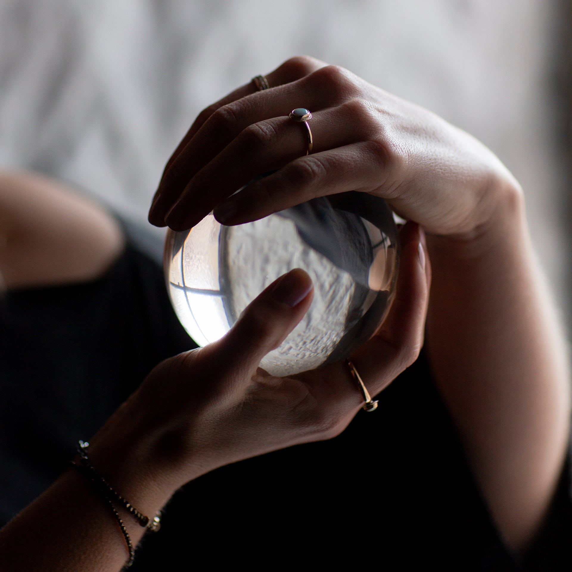 Two hands, each wearing gold opal rings, holding a crystal ball.