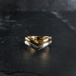 Two wishbone style wedding rings, one yellow gold and the other Sterling Silver sit nested together on with a dark textured slate surface. Handmade by Emily Eliza Arlotte in Hobart, Tasmania.