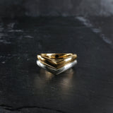 Two wishbone style wedding rings, one yellow gold and the other Sterling Silver sit nested together on with a dark textured slate surface. Handmade by Emily Eliza Arlotte in Hobart, Tasmania.