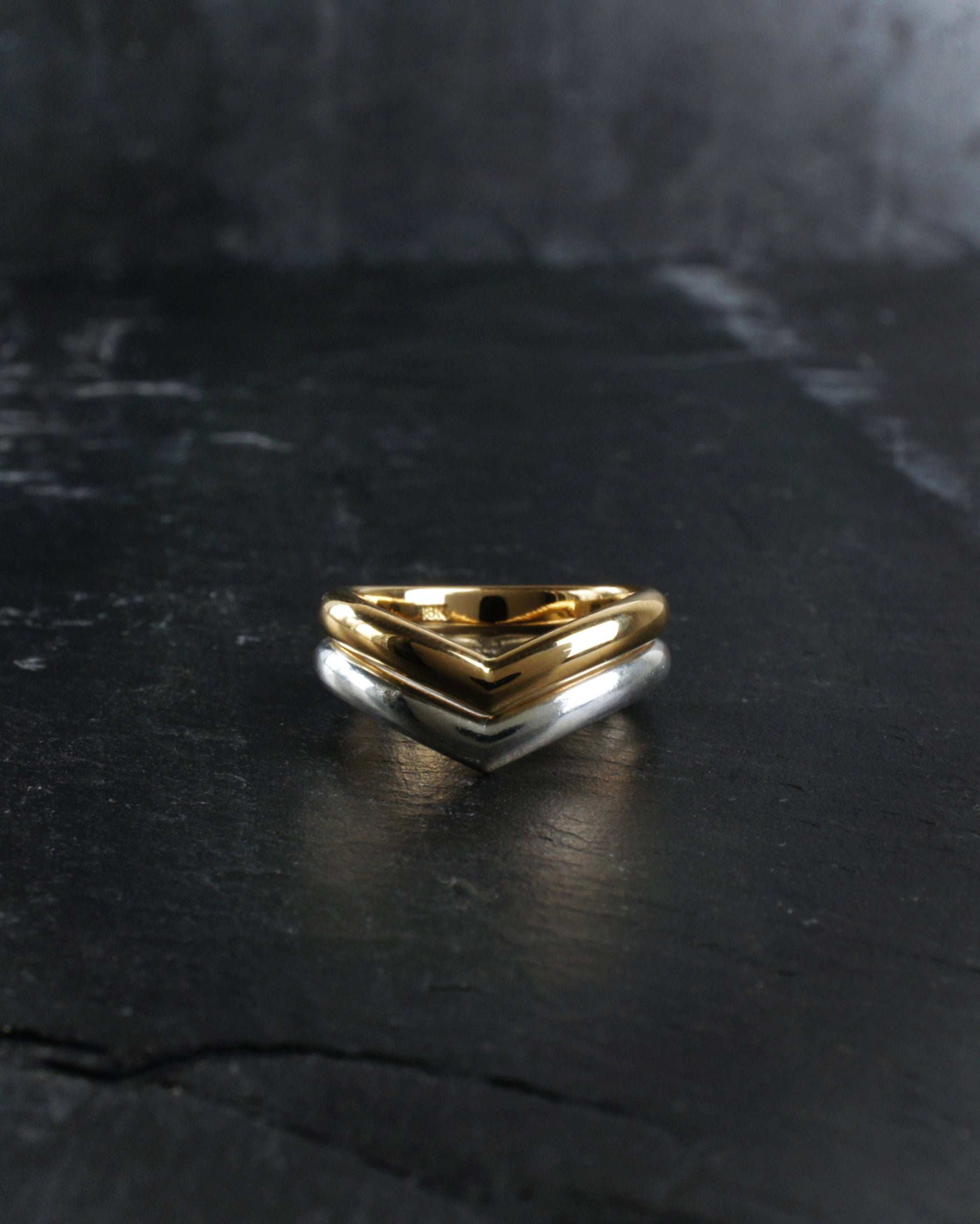 Two wishbone style wedding rings, one yellow gold and the other Sterling Silver sit nested together on with a dark textured slate surface. Handmade by Emily Eliza Arlotte in Hobart, Tasmania.
