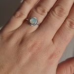 A handmade sterling silver ring featuring an Australian Crystal Opal from Coober Pedy. The opal features pinks, greens, and blue swirls of colour and is set in a radiant engraved silver setting. It is being worn by a hand and is showing off the play of colours in the sun.