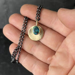 A hand is holding an Australian Black opal and Gold pendant that hangs on an oxidised sterling silver chain. The movement in the video shows off the the blue, green, and black swirls in the opals as well as the intricate engraved detail of the pendant.