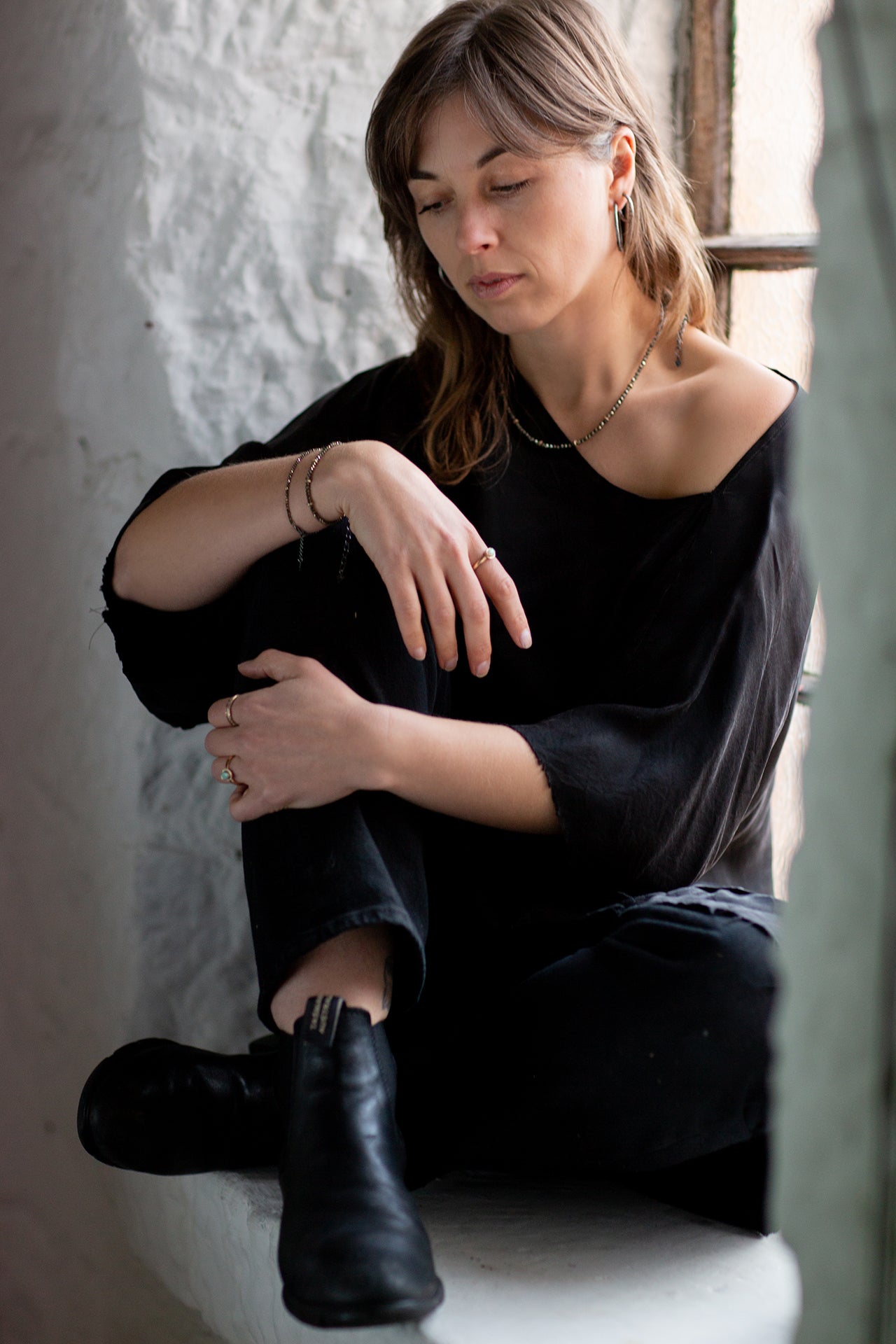  Model Eden is shown sitting in a window seal  wearing the faceted Pyrite and Gold beaded choker necklace with oxidised sterling silver chain. Handmade by Emily Eliza Arlotte in Hobart, Tasmania. Photography by Cassie Sullivan