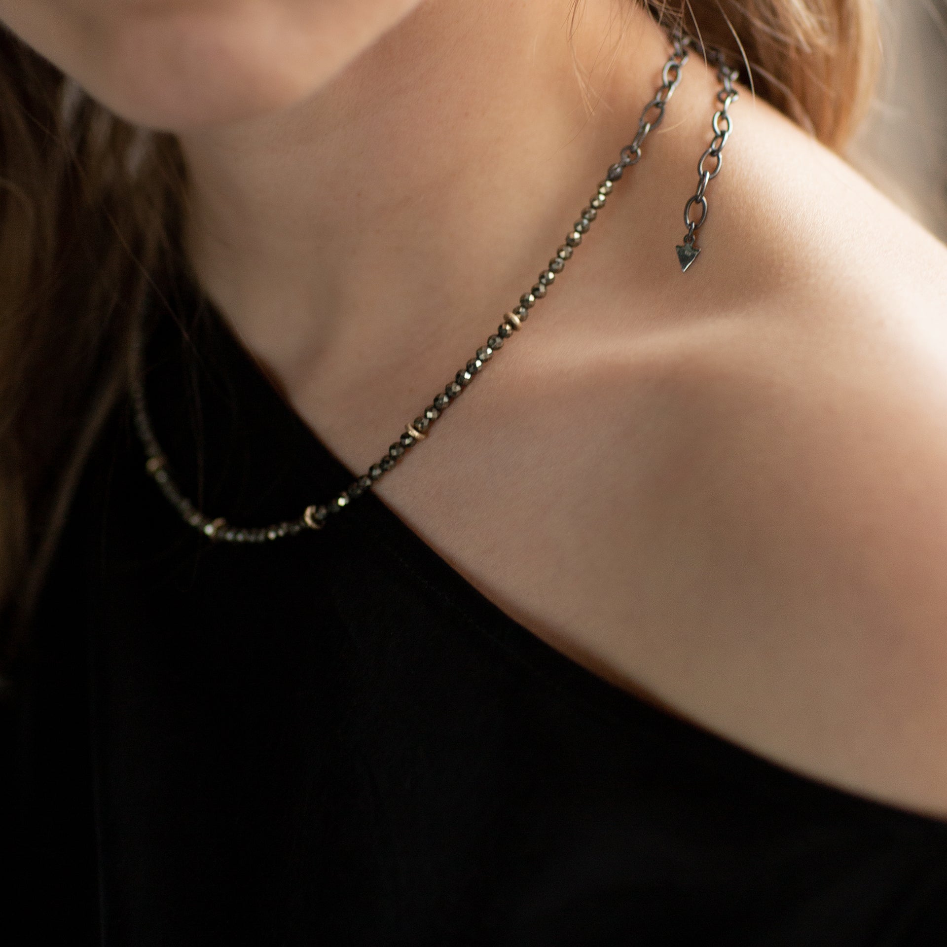 The neck and shoulder of model Eden is shown wearing the faceted Pyrite and Gold beaded choker necklace with oxidised sterling silver chain. Handmade by Emily Eliza Arlotte in Hobart, Tasmania. Photography by Cassie Sullivan.