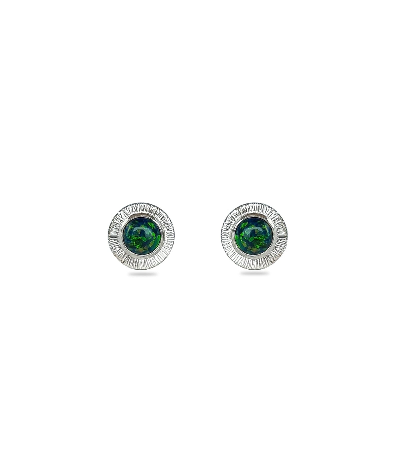 A pair of handmade opal stud earrings by Emily Eliza Arlotte, featuring forest green opals and an engraved textured halo, on a white background.