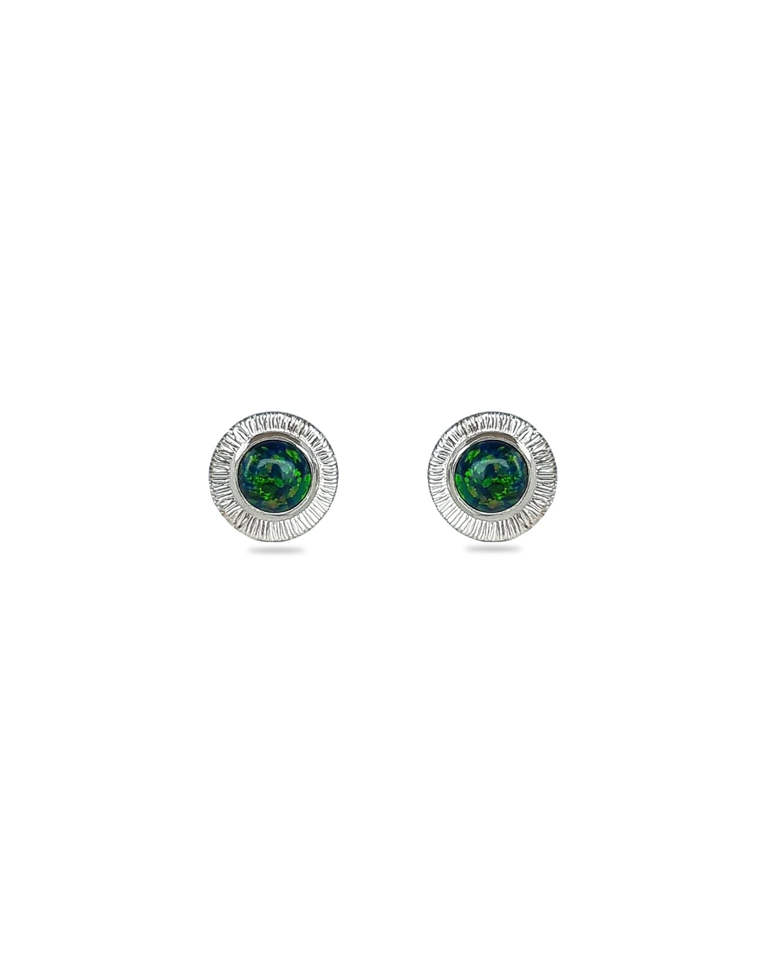 A pair of handmade opal stud earrings by Emily Eliza Arlotte, featuring forest green opals and an engraved textured halo, on a white background.