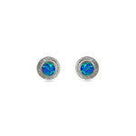 A pair of handmade opal stud earrings by Emily Eliza Arlotte, featuring bright blue opals and an engraved textured halo, on a white background.