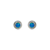 A pair of handmade opal stud earrings by Emily Eliza Arlotte, featuring bright blue opals and an engraved textured halo, on a white background.