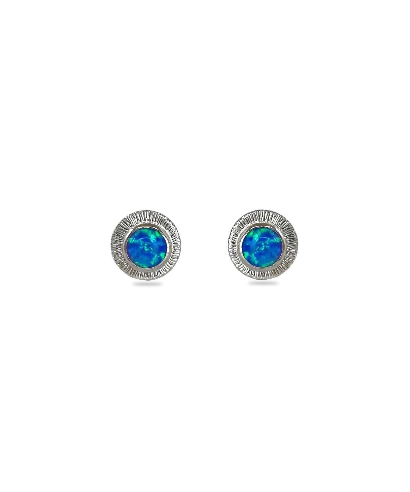 A pair of handmade opal stud earrings by Emily Eliza Arlotte, featuring bright blue opals and an engraved textured halo, on a white background.