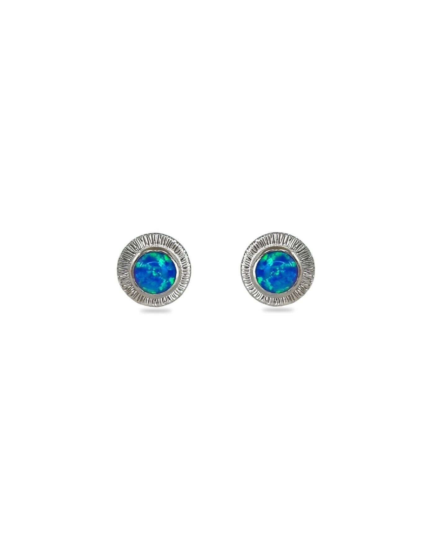 A pair of handmade opal stud earrings by Emily Eliza Arlotte, featuring bright blue opals and an engraved textured halo, on a white background.