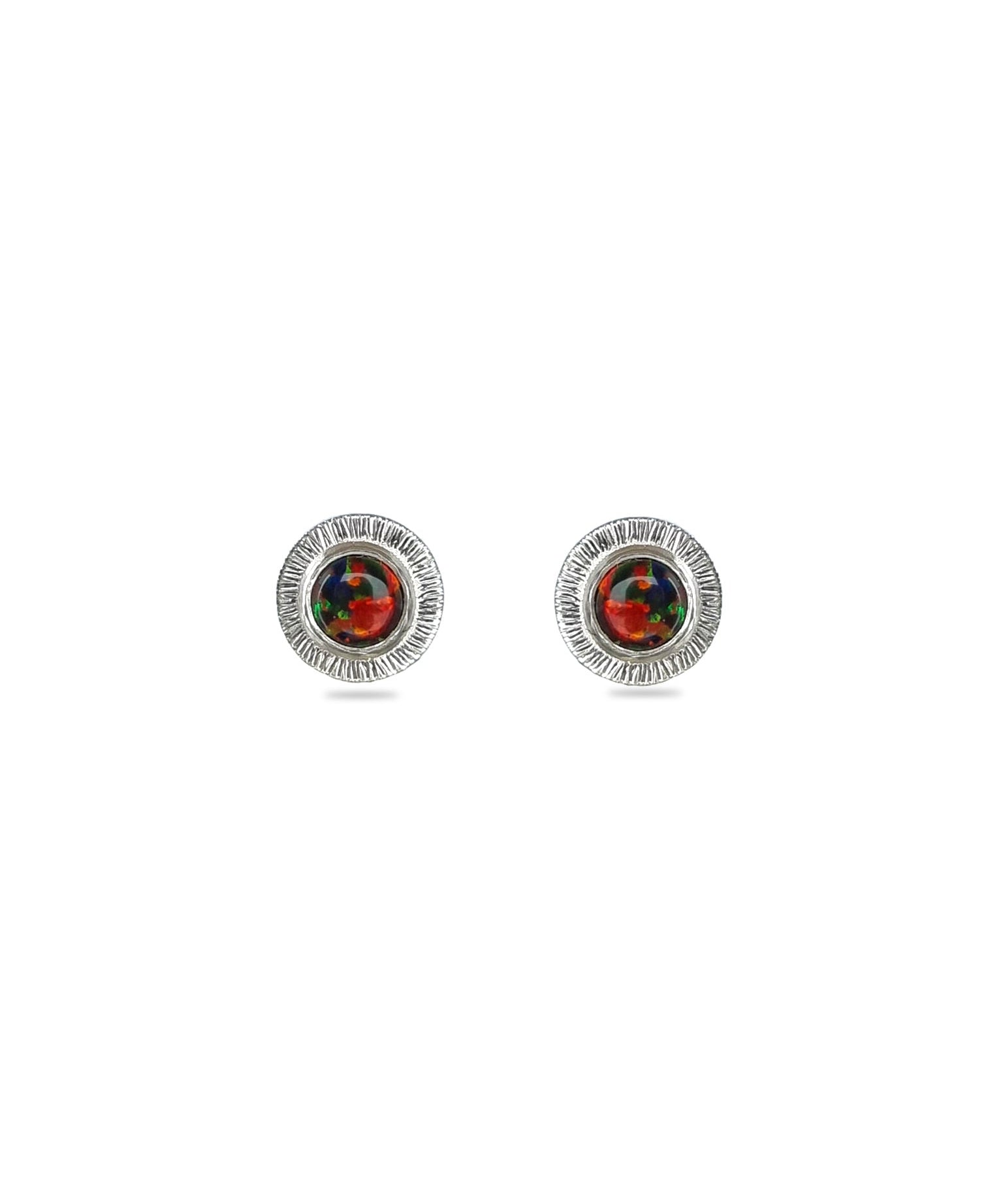 A pair of handmade opal stud earrings by Emily Eliza Arlotte, featuring red and black opals and an engraved textured halo, on a white background.