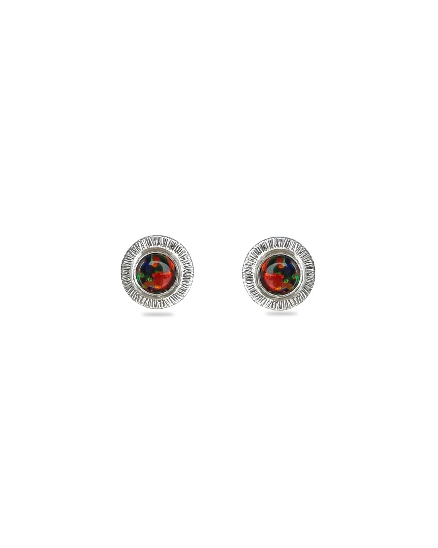 A pair of handmade opal stud earrings by Emily Eliza Arlotte, featuring red and black opals and an engraved textured halo, on a white background.