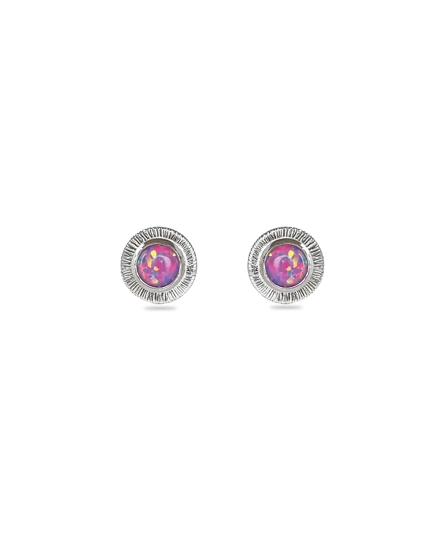 A pair of handmade opal stud earrings by Emily Eliza Arlotte, featuring violet purple opals and an engraved textured halo, on a white background.