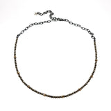 A beaded Pyrite and 9ct Gold choker necklace hangs on a white background. It has a blackened sterling silver chain. Handmade by Emily Eliza Arlotte Handcrafted Fine Jewellery in Hobart, Tasmania Australia.
