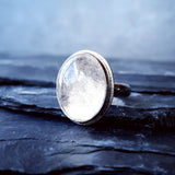 A large quartz stone set in the Prescience Ring by Emily Eliza Arlotte sits sidways on layers of dark slate stone.