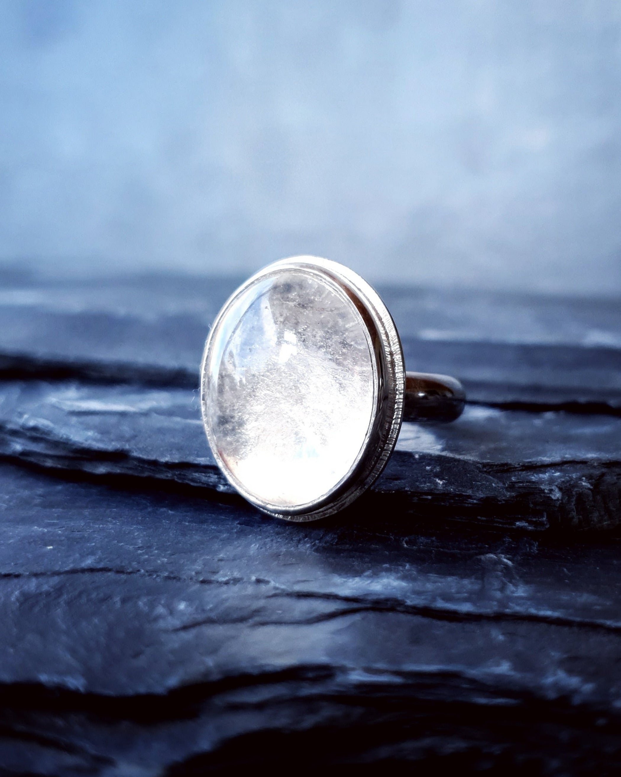 A large quartz stone set in the Prescience Ring by Emily Eliza Arlotte sits sidways on layers of dark slate stone.