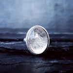 A large quartz stone set in the Prescience Ring by Emily Eliza Arlotte sits on layers of dark slate stone.
