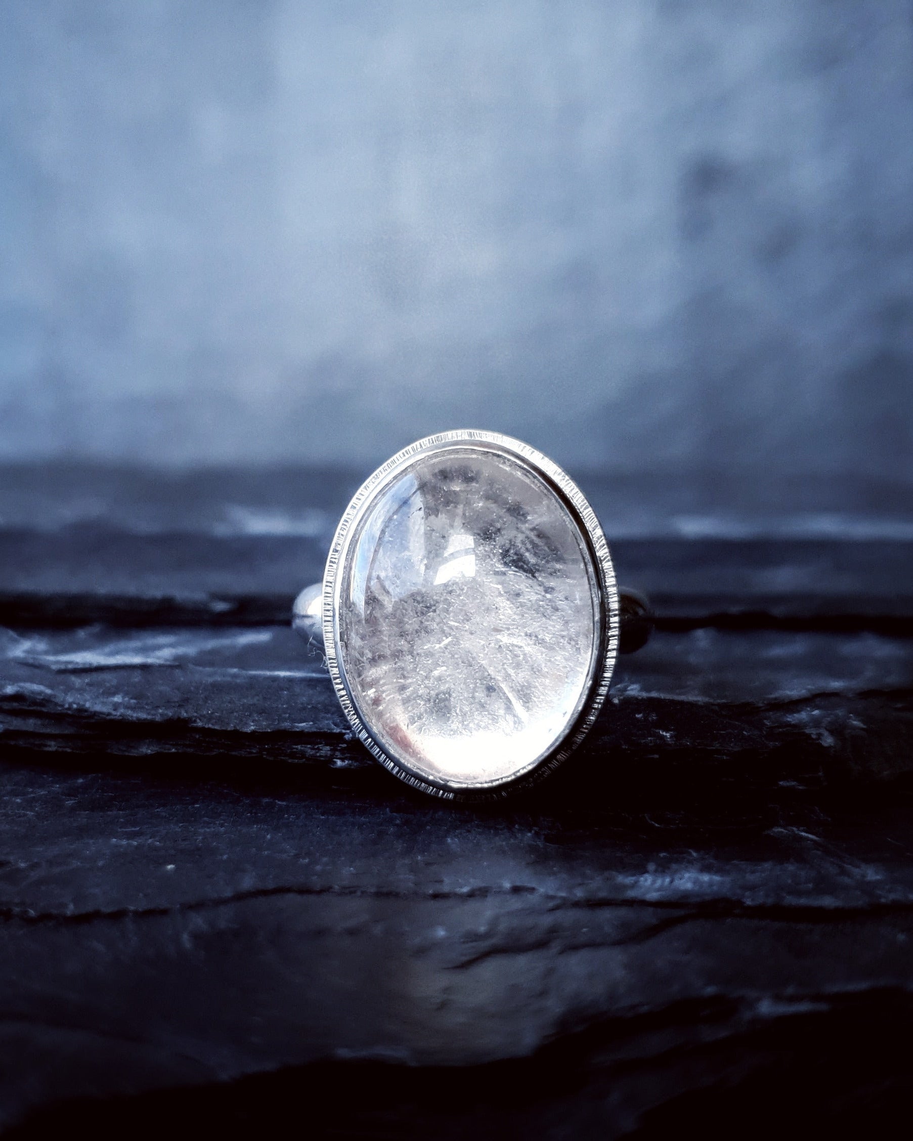 A large quartz stone set in the Prescience Ring by Emily Eliza Arlotte sits on layers of dark slate stone.