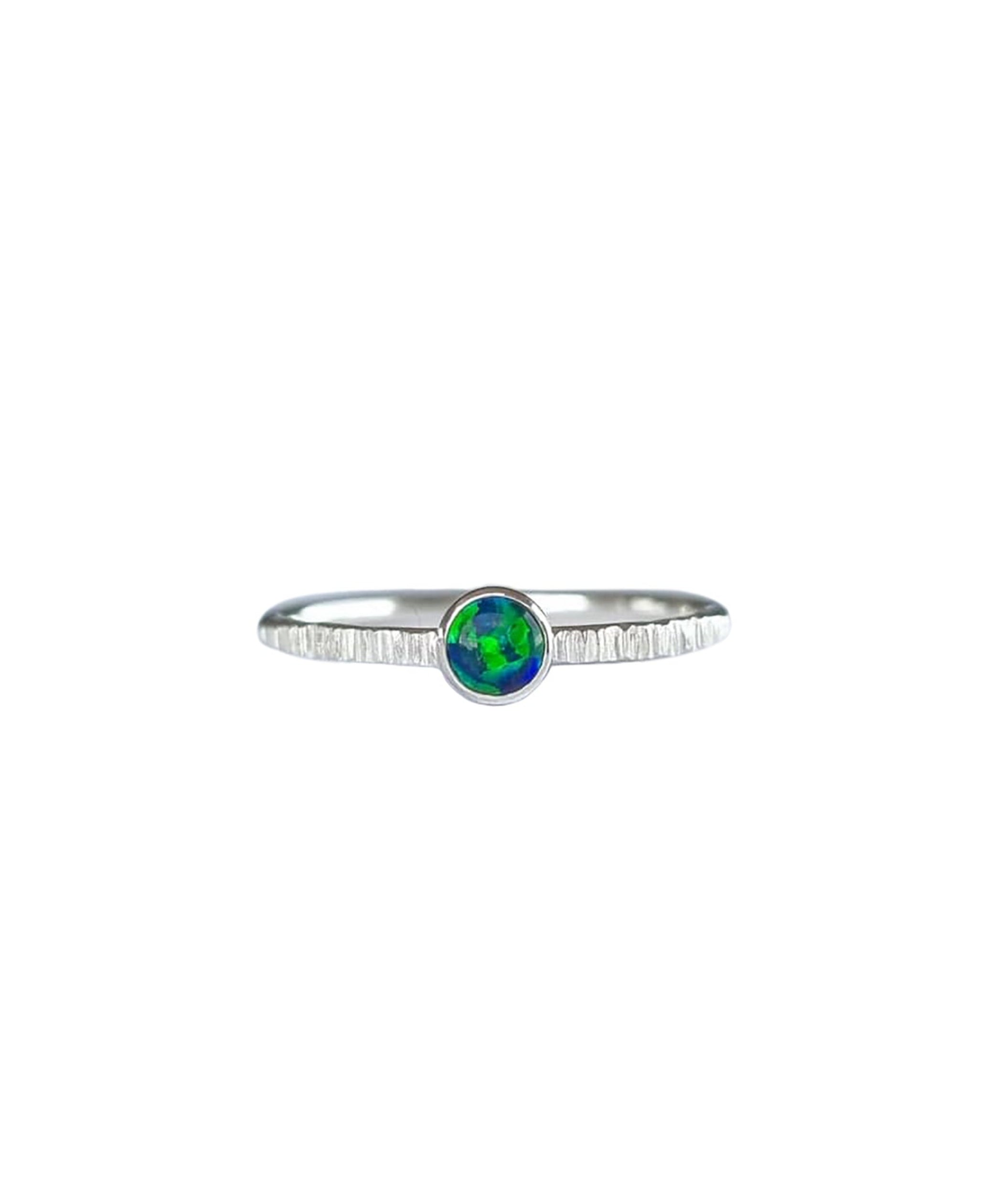 A Sterling Silver Opal Ring, with a subtle texture on a fine band sits on a background of white. The opal is a deep forest green colour with shifting dark blue flashes.