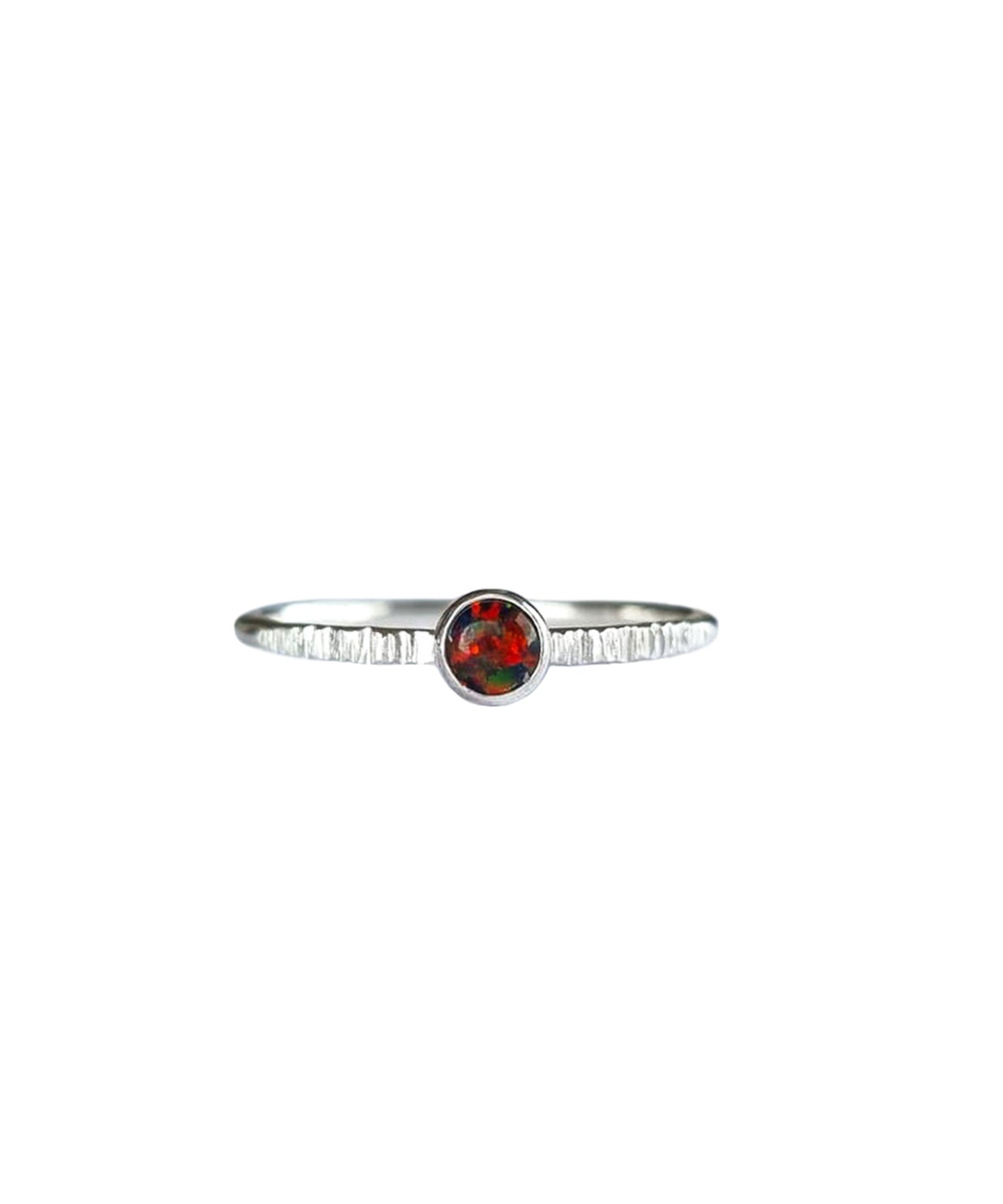 A Sterling Silver Opal Ring, with a subtle texture on a fine band sits on a background of white. The opal is a deep molten red colour with shifting black and dark green flashes.