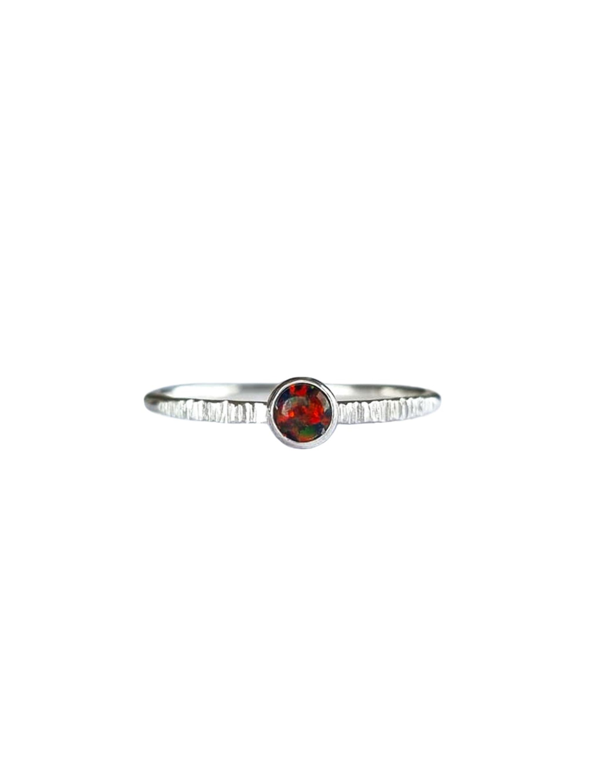 A Sterling Silver Opal Ring, with a subtle texture on a fine band sits on a background of white. The opal is a deep molten red colour with shifting black and dark green flashes.