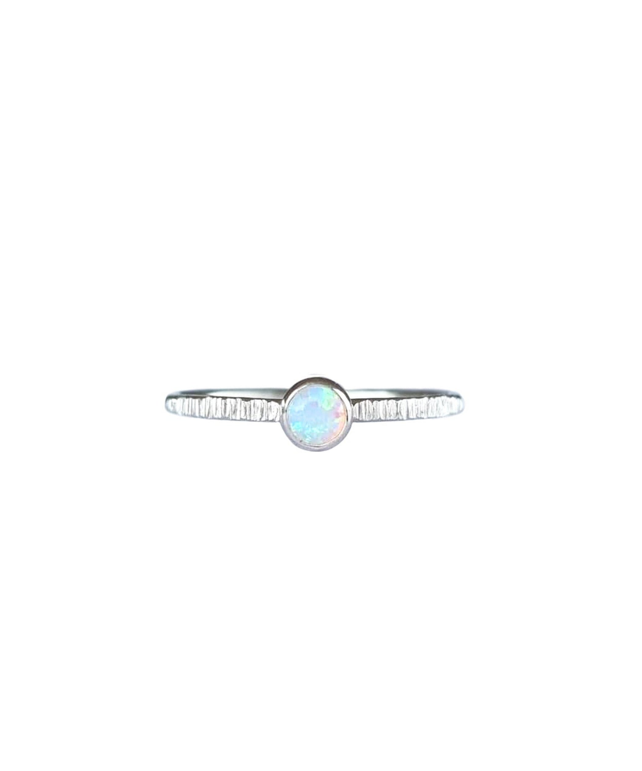 A Sterling Silver Opal Ring, with a subtle texture on a fine band sits on a background of white. The opal is an opalescent colour of shifting pinks and blues.