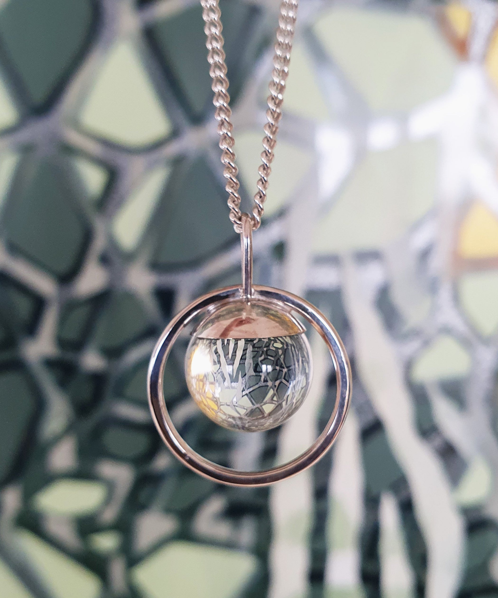 The Divination Necklace, handmade by Emily Eliza Arlotte, features a clear quartz sphere reflecting and inverting the image of an artwork by Jamin Kluss behind it.