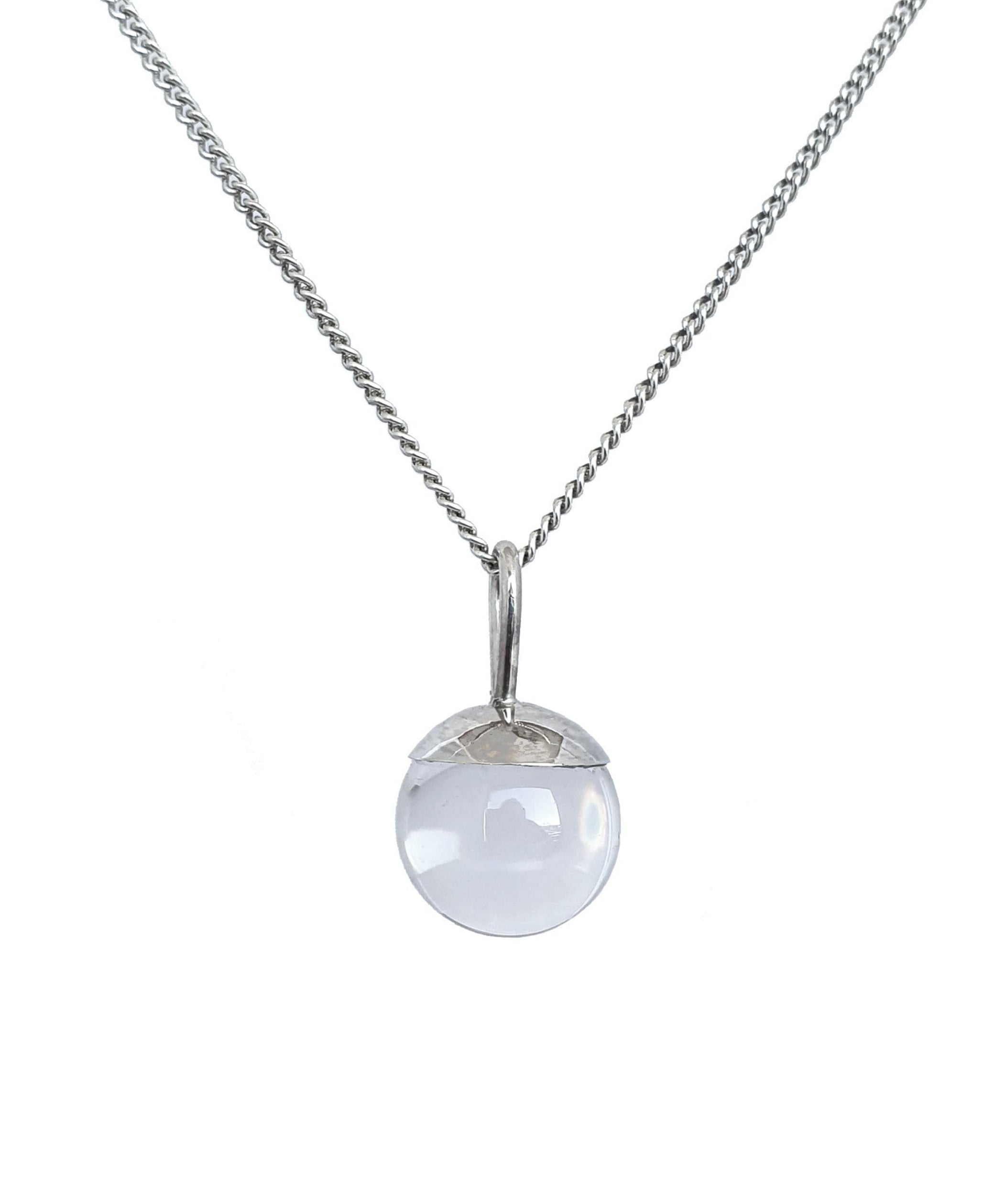 The Divination Orb Necklace hangs on a background on white. The sterling silver pendant necklace features a quartz crystal ball, and is handmade by Emily Eliza Arlotte in Hobart, Tasmania.