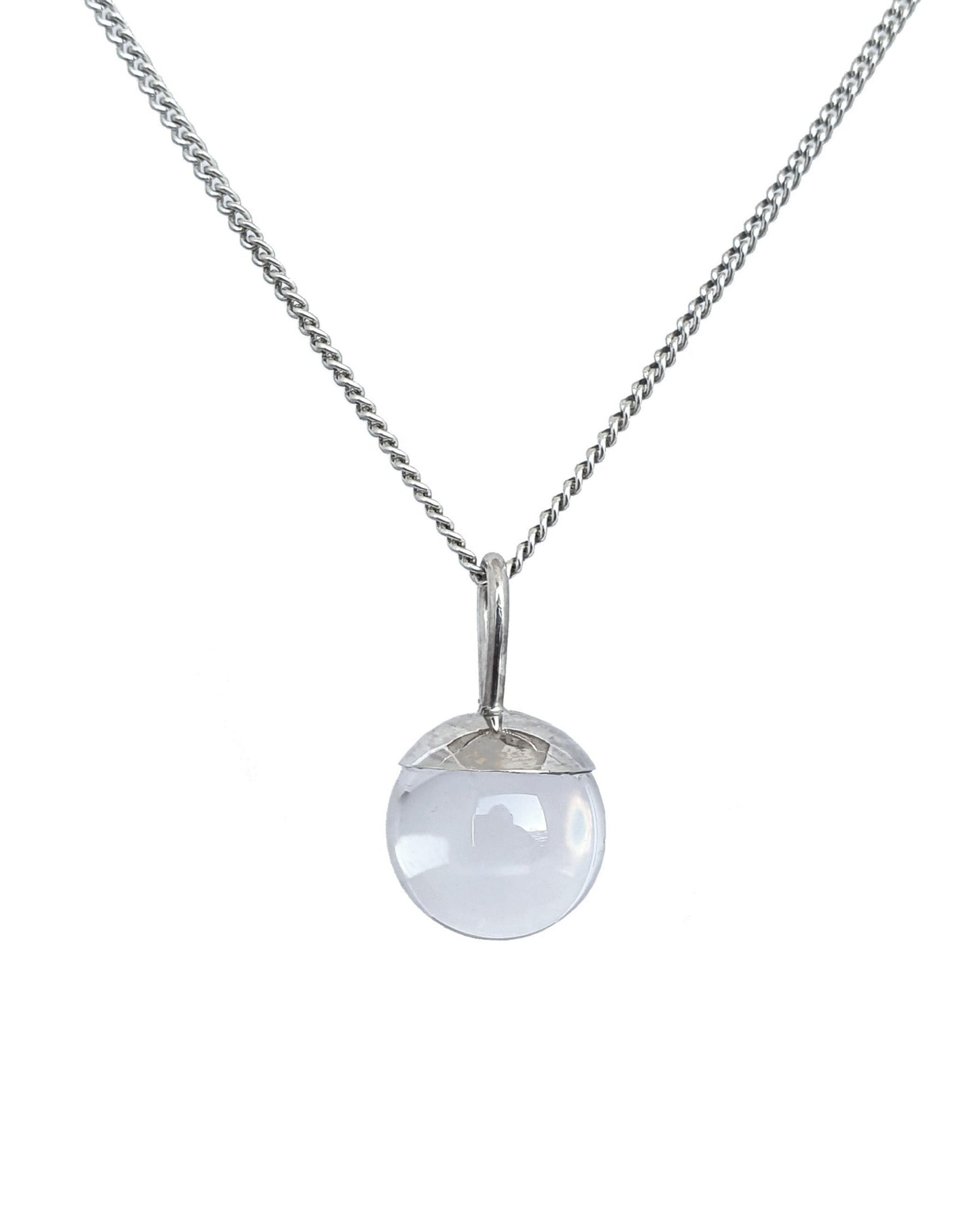 The Divination Orb Necklace hangs on a background on white. The sterling silver pendant necklace features a quartz crystal ball, and is handmade by Emily Eliza Arlotte in Hobart, Tasmania.